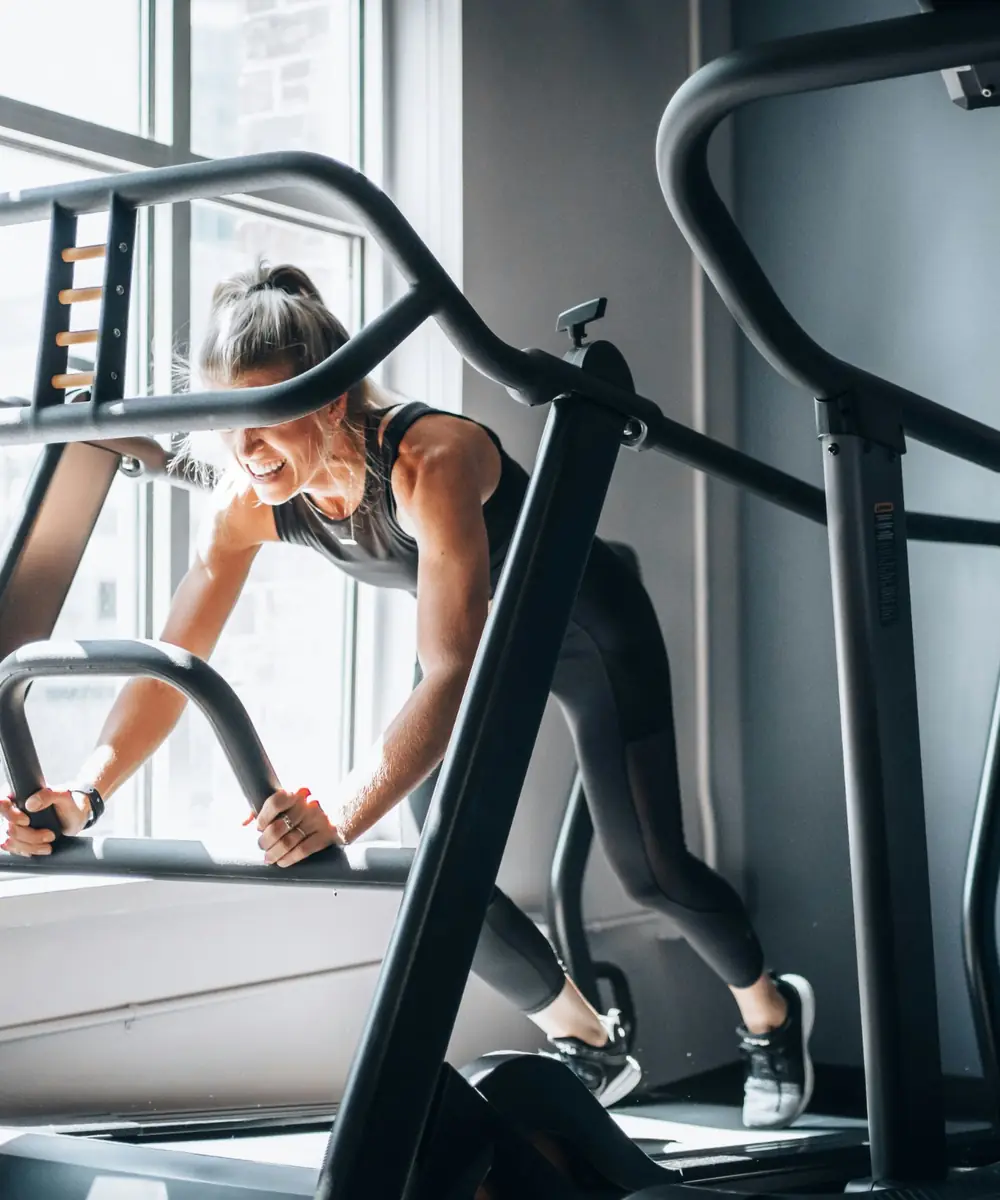 Mujer entrenando en una máquina de cardio junto a la ventana de un gimnasio